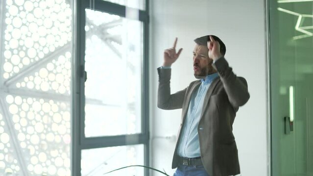 Happy joyful businessman dancing in corridor or hall of modern business center. Excited man office worker cheerfully celebrating achievement, rejoices in success. Victory dance of a funny employee