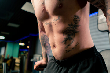 close-up in the gym of the torso of a young handsome guy with tattoos of the abs and pectoral...