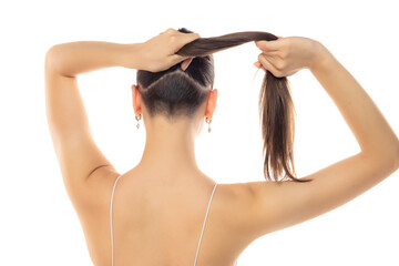 Rear view of a young modern woman with partially shaved head and ponytail on a white background