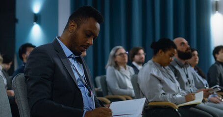 Multiethnic journalists sit and write answers from organization representative during press...