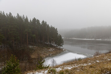 Fototapeta premium river bank and water in winter in foggy weather