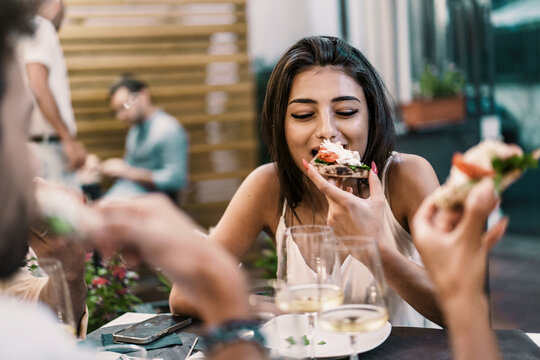 A young woman savoring a delicious pizza slice, enjoying an al fresco dining experience with friends at an ambient restaurant. - Powered by Adobe
