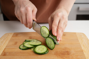 Woman's hand cutting cucumbers, kitchen cooking, vegetable slicing, salad preparation.