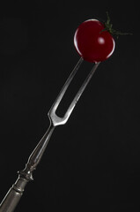 Cherry tomato prickled by a vintage fork on black background
