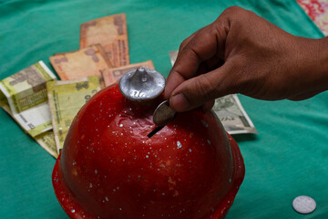 Indian male dropping cash into traditional clay pot or Gullak or piggybank. Family savings, financial education concept.