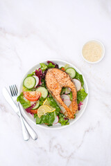 Grilled salmon and fresh vegetables: tomatoes, cucumber, lemon, radish on marble background.