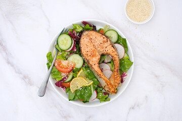 Grilled salmon and fresh vegetables: tomatoes, cucumber, lemon, radish on marble background.