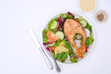 Grilled salmon and fresh vegetables: tomatoes, cucumber, lemon, radish on white background.