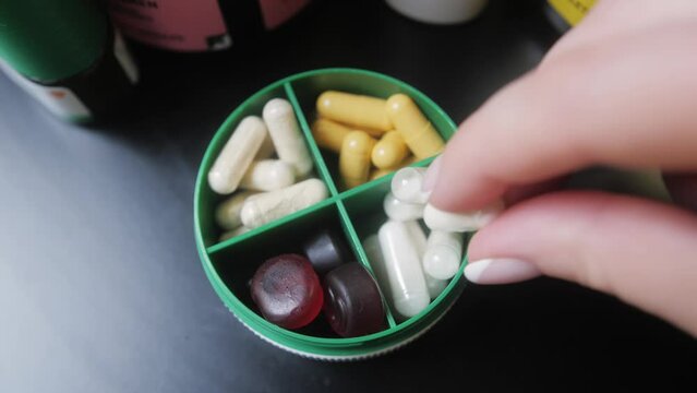 Hands takes pills from pill box, close-up. Medical pill box with doses of tablets for daily take medicine with drugs and capsules.