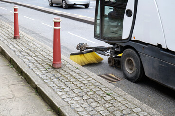 Road sweeper cleaning tarmac using a yellow bristle brush to clean the surface. - obrazy, fototapety, plakaty