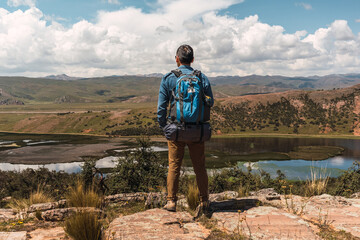 mountaineer with blue backpack standing on the rock in latin america in the andes mountain range with view of lake and mountains with blue sky with clouds