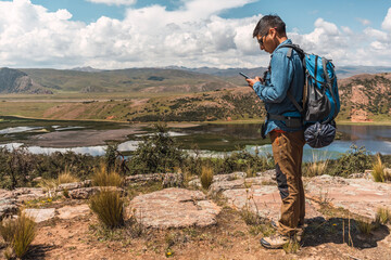 mountaineer with blue backpack standing in profile with cell phone in hand on the rock in Latin...