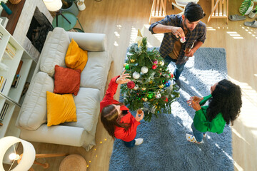 Multi-ethnic group enjoying the holiday season, decorating a lush Christmas tree and sipping on...