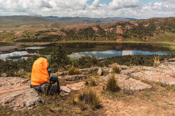 orange hiking backpack placed on the rocks in the mountain surrounded by green vegetation and...