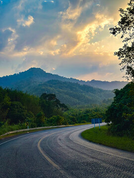 A tranquil highway leads towards a stunning sunset, flanked by lush greenery and radiant skies at dusk.