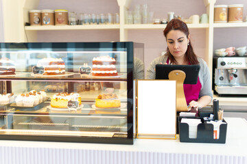 Fototapeta na wymiar red-haired waitress at the counter of her cafeteria pastry shop enters the amount into her computer to charge for handmade cake