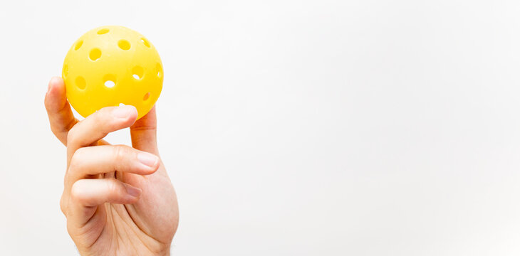 Photograph of a hand on a white studio background clutching a yellow pickleball ball. Pickleball concept. Copyspace for advertising and advertisements.