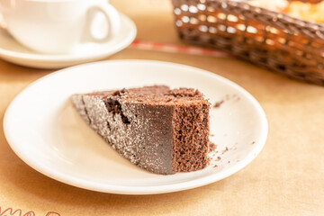 Fototapeta na wymiar Piece of fresh homemade chocolate sponge cake on white plate, cup of tea or coffee on laid table
