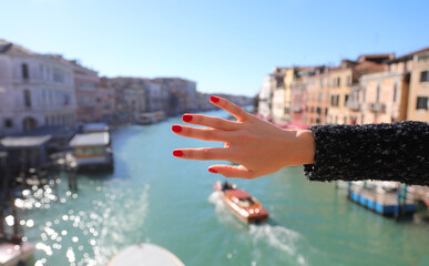 Hand of girl with slender fingers and red-polished nails and Venice Grand Canal with boats
