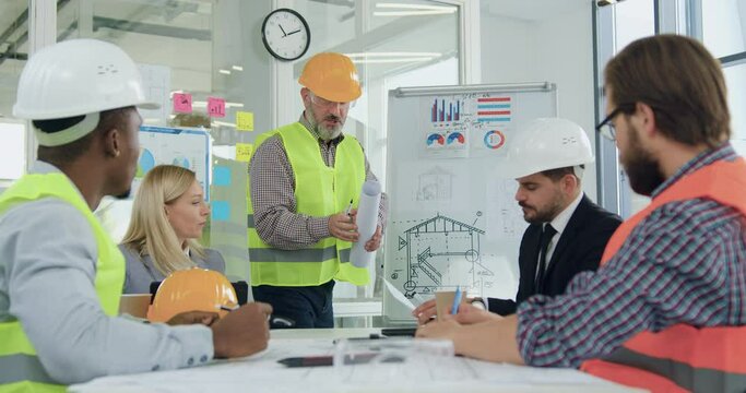 Multiracial team of engineers and chiefs revision ready building drawing during briefing in meeting room