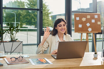 A businesswoman in a modern office sits in front of a laptop, deep in thought as she works on a...