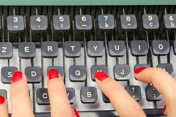 polished fingernails of secretary typing on the keys of an old typewriter in an office