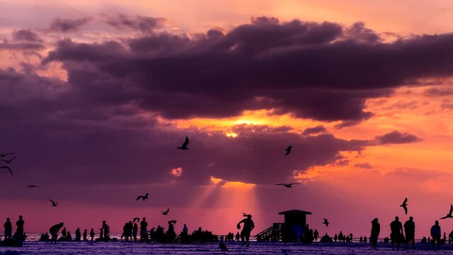 Crowd of people enjoy beach holiday during dramatic sunset