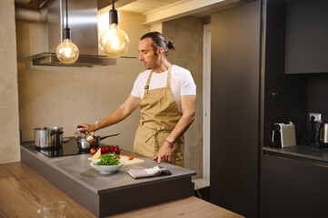 Handsome man cooking healthy dinner in modern kitchen interior. attractive guy, chef in beige...