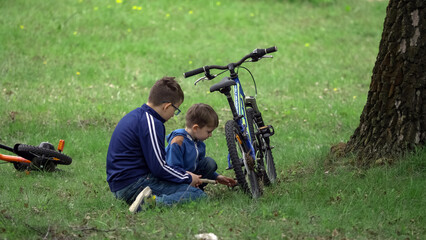 Big brother helps little kid to repair the bike in the forest