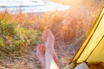 Women legs peek out from a tourist tent at dawn, on the seashore. Travel and outdoor recreation