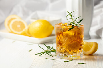 Iced tea or alcoholic cocktail with ice, rosemary and lemon slices on the white table.