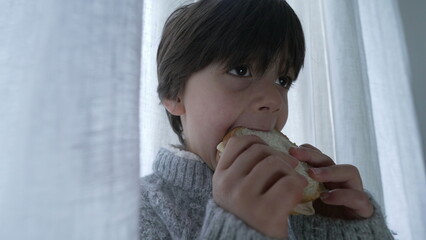 Child snacking sandwich, close-up hand and face of one small boy eating rich carb food in the...