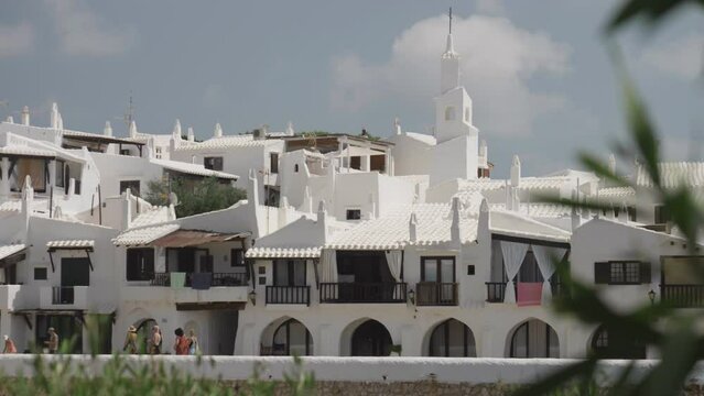 Spectacular view of Binibeca Vell town in the Spanish Menorca Island, with its whitewashed houses with wooden windows, around the church belfry and surrounded by lush vegetation, Menorca Island, Spain