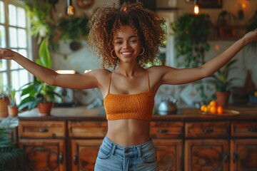 Woman in crop top and jeans with arms outstretched in kitchen - obrazy, fototapety, plakaty