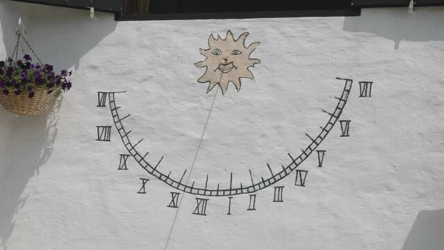 Sundial with hours painted on wall with wooden stick shadow indicating the time of the day, an old rustic solar clock on whitewashed wall of a house in Binibeca Vell, Menorca, Spain