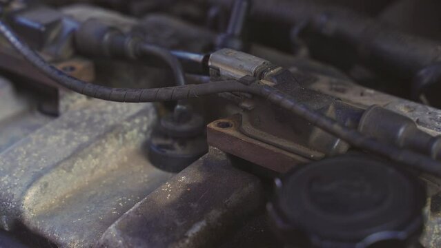 A male mechanic unscrews mounting bolts and replaces the ignition coil on a car engine. Close-up.