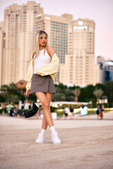 A woman poses wearing a stylish outfit against an urban background at sunset