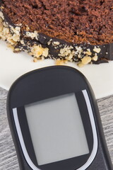 Glucometer for measuring sugar level and sweet chocolate cake. Nutrition during diabetes