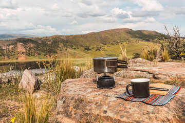 set of camping utensils pots knife knife cup and chopping board placed on the vegetation in the Andes mountain range with a lake background and blue sky with clouds