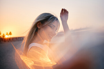 Against a soft-focus sunset, the silhouette of a woman raises her hand in a peaceful gesture,...