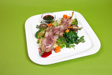 delicious ribs with vegetables and mushrooms on a white plate on a green background