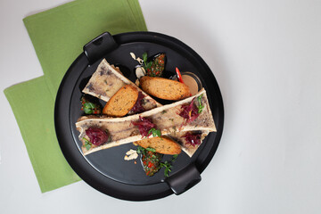 delicacy top view, baked bone marrow with croutons, herbs and spices on a black plate
