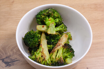 The white bowl with stir-fried broccoli on the wooden table 