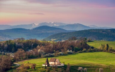 Fototapeta na wymiar Picturesque spring mountain landscape with hills, meadows and romantic historic wooden building at colorful sunset. The village of Cerin near Banská Bystrica, Slovakia