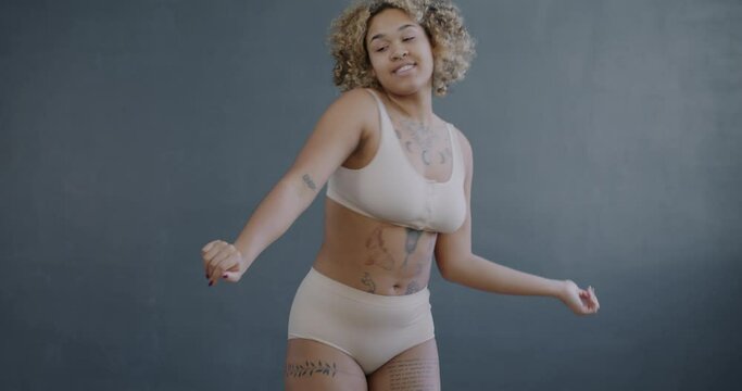 Slow motion portrait of carefree African American woman wearing underwear dancing on gray color background. Body positive lady and entertainment concept.