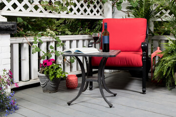 A black metal chair with red cushions and a wrought metal table with a bottle of wine and glass of wine on a verandah - obrazy, fototapety, plakaty
