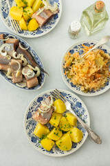 Delicious hearty fish dinners, boiled potatoes with pickled herring, sauerkraut with onions and olive oil, top view