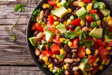Cowboy bean salad with black beans tomatoes avocado red bell pepper corn and coriander in a black bowl on a dark wooden table close up - Powered by Adobe