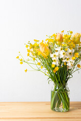 Spring bouquet of yellow buttercups, white daffodils and tulips, bouquet of flowers on the table near the wall, home decoration with flowers