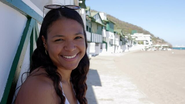 Portrait of a happy hispanic latin woman on the beach smiling at camera. Holiday lifestyle, summertime and travel vacation concept.